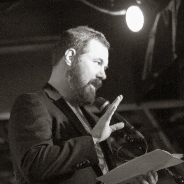 The author, under stage lights, speaks into a microphone